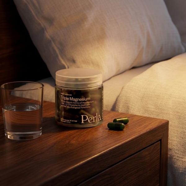 A high-quality 1:1 image featuring a jar of Triple Magnesium supplements, a glass of water, and capsules on a wooden nightstand in warm, dim lighting.